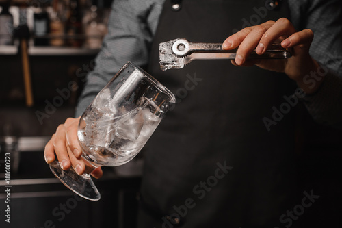 Barman in the apron putting ice cubes into the cocktail glass