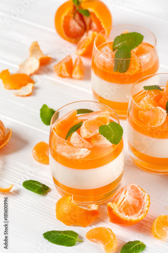 Creamy panna cotta with orange jelly in beautiful glasses, fresh ripe mandarin, on white wooden background. Delicious Italian dessert. Closeup photography. Selective focus.
