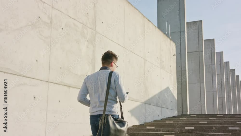 A young man walking and using a smartphone outside. Medium Dolly shot A young man walking and using a smartphone outside. Medium Dolly shot