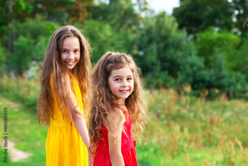 Obraz premium Two beautiful little girls embracing and smiling at sunny summer day. Happy childhood concept