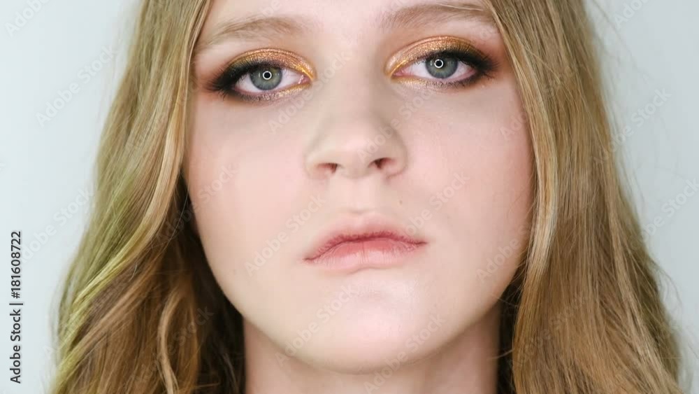 Close up portrait of beautiful young woman face with bright bronze make up looking at camera, then in front. Girl showing eye make-up