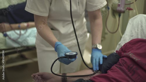 Caucasian charming nurse measures blood pressure of patient during hemodialysis treatment at hospital room, tilt up from male hand to portrait of woman, close up, shallow depth of field, real scene photo