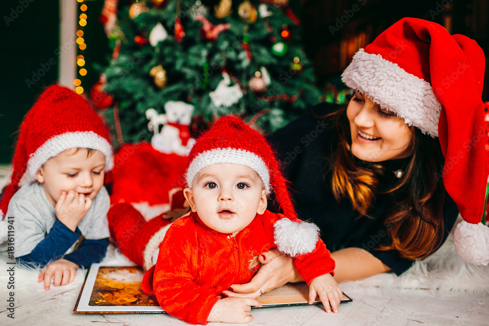 Mom and her sons in red hats lie before Christmas tree Mom and her sons in red hats lie before Christmas tree