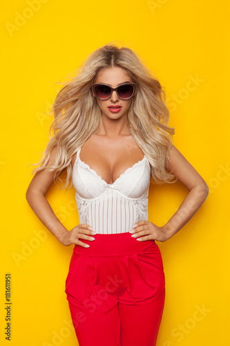 Sexy Blond Woman In White Corset And Red Pants Is Posing With Hands On Hip