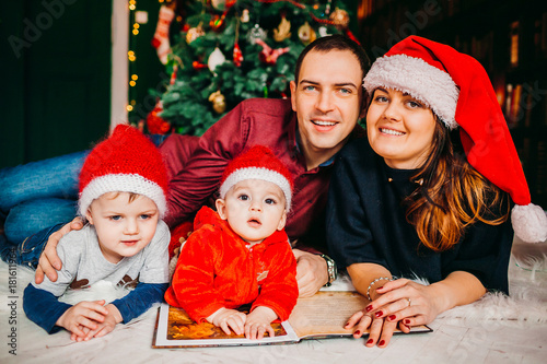Mom, dad and their sons in red hats lie before Christmas tree