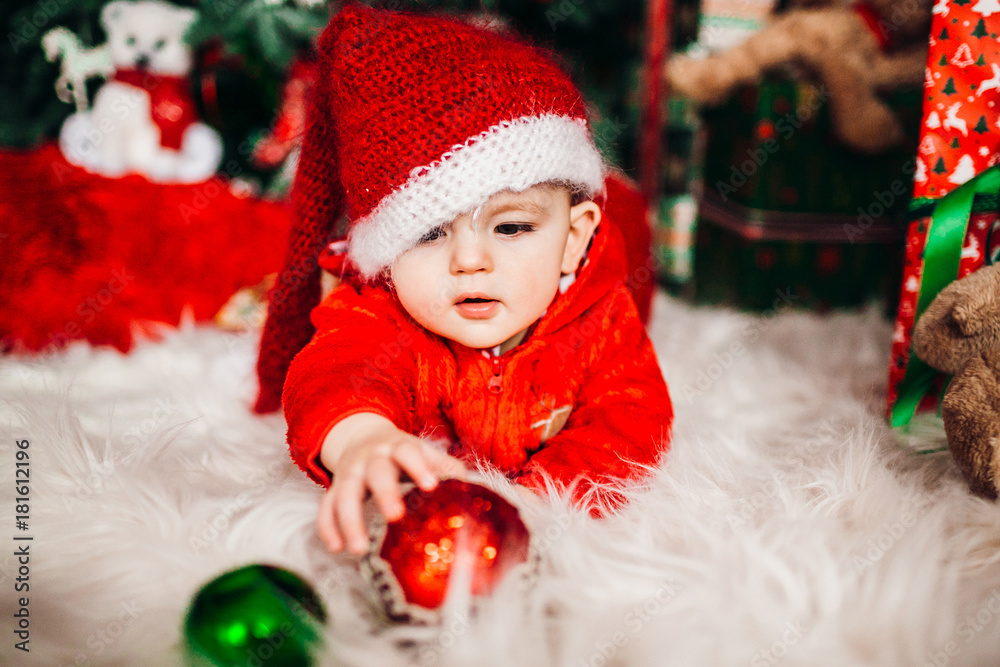 Pretty little boy in red suit lies on fluffy carpet before a Christmas tree Pretty little boy in red suit lies on fluffy carpet before a Christmas tree