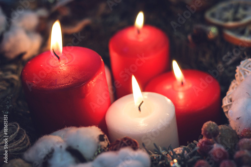 Four burning christmas candles in a wreath with natural decorations closeup