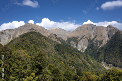 Azerbaijan, Greater Caucasus, near Gabala, Durca: Scenic panoramic view with rocky mountain chain, green trees, blue sky and white clouds.