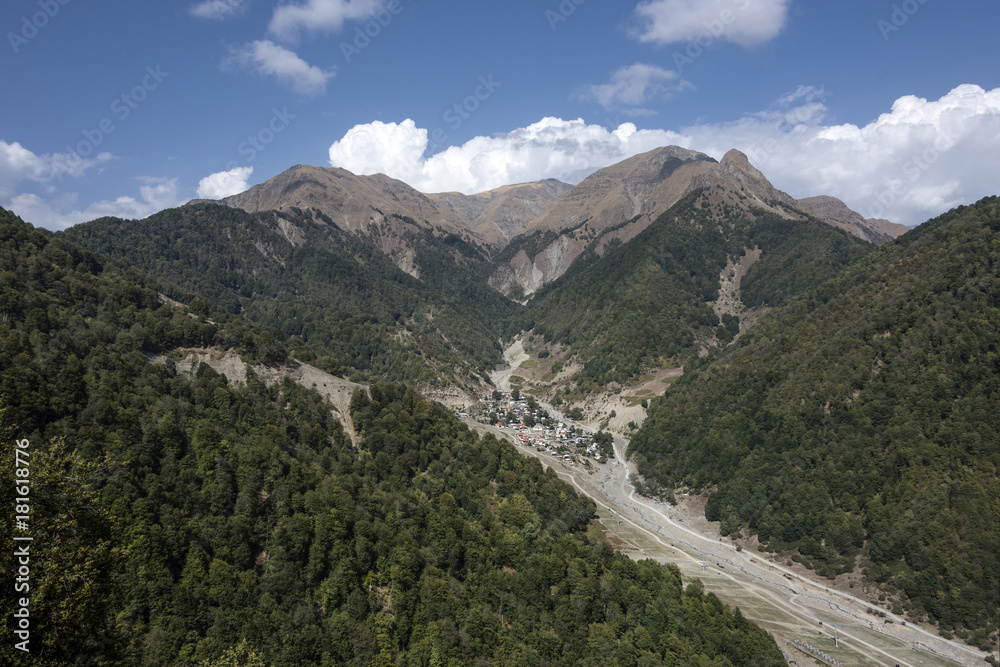 Azerbaijan, Greater Caucasus, near Gabala, Durca: Scenic panoramic view with village, gorge, rocky mountain chain, green trees, blue sky and white clouds. 