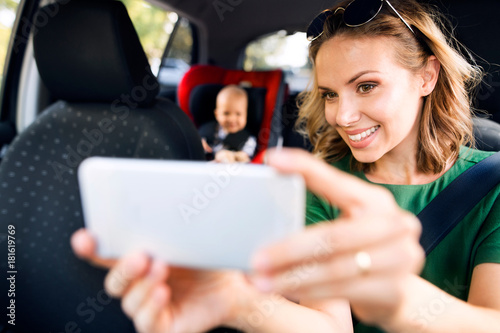 Young mother with smartphone and baby boy in the car.