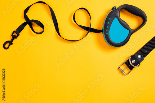 Black leather dog collar and blue leash attached on yellow background. Top view photo