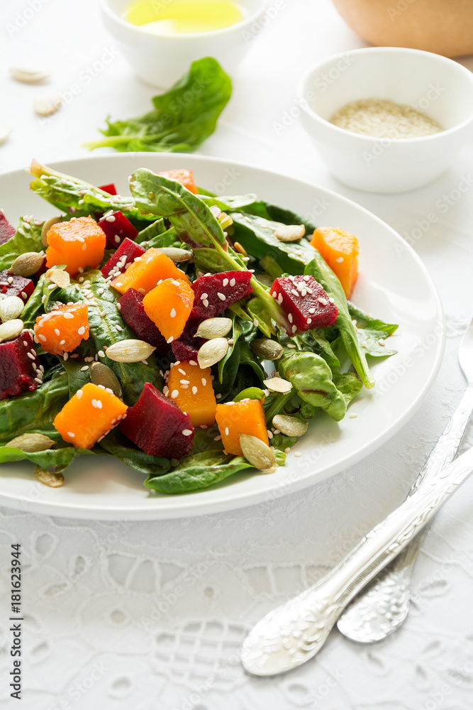 Fresh autumn salad with marinated pumpkin and beetroot, spinach leaves,olive oil, sesame and pumpkin seeds on white table cloth. Space for copy