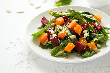 Fresh autumn salad with marinated pumpkin and beetroot, spinach leaves,olive oil, sesame and pumpkin seeds on white table cloth. Space for copy