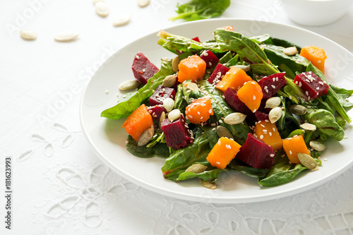 Fresh autumn salad with marinated pumpkin and beetroot, spinach leaves,olive oil, sesame and pumpkin seeds on white table cloth. Space for copy