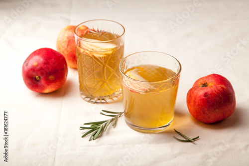 Two vintage glasses with apple cider on black background. Christmas beverages concept. Two red apples and rosemary sprig aside.  Warm backlight.