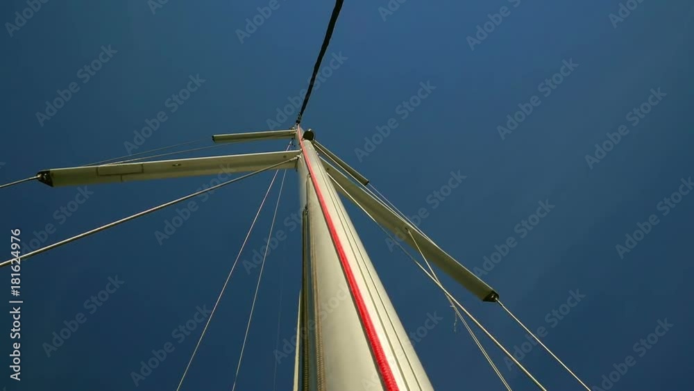Sailing boats main mast with windex and supporting steel ropes. Shot from start of the mast looking upwards to blue sky.