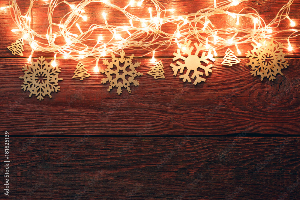 Obraz premium Photo of New Year's wooden red background with burning garland from above, snowflakes
