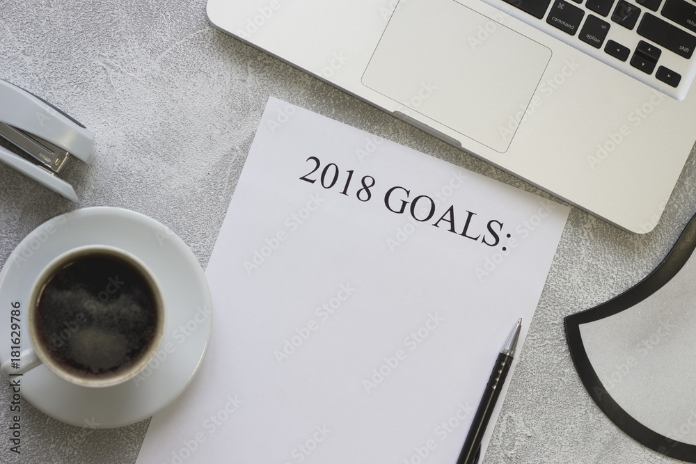 2018 goals paper with a cup of coffee, a laptop and office supplies on a light concrete background, top view 2018 goals paper with a cup of coffee, a laptop and office supplies on a light concrete background, top view