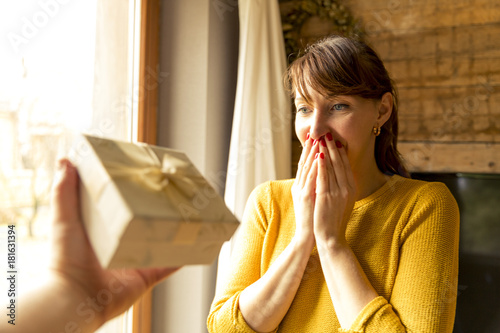 happy woman receiving a gift from husband by a window photo