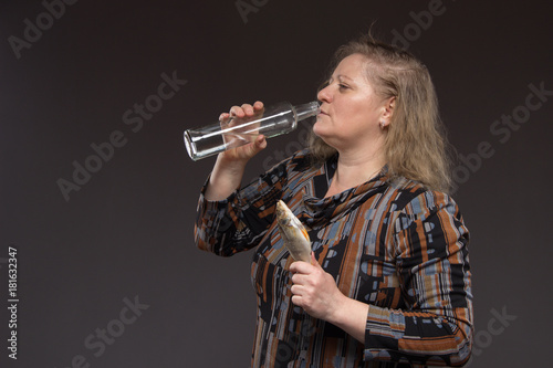 Lonely mature fat woman alcoholic drinks vodka from glasses and wine glasses and snack cucumber and fish