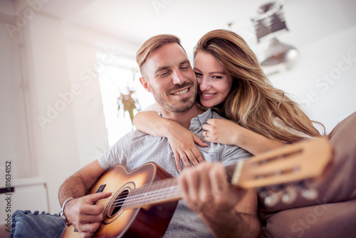 Beautiful loving couple playing guitar in the living room at home.