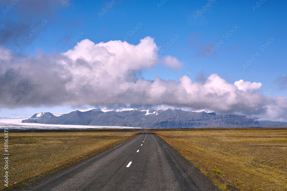 Travel to Iceland. road in a bright sunny mountain landscape. Vatna volcano covered with snow and ice on tne background.