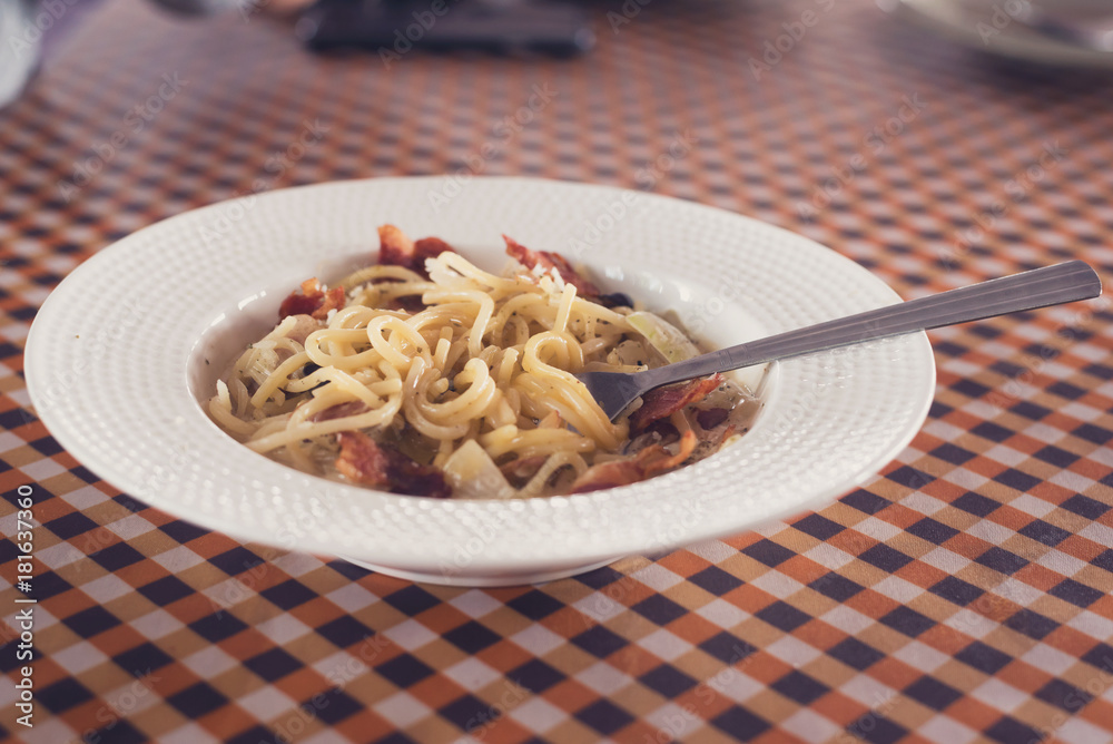 The spaghetti carbonara with a spoon in a dish on the dinner table.