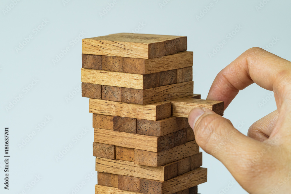 Risk or stability concept as female hand pulling wooden block from the tower Risk or stability concept as female hand pulling wooden block from the tower