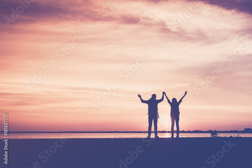 Silhouette of couple hikers with arms raised up and backpacks, relaxing and freedom between on walking on the Beach road at sunset. The concept of lovers and tourist traveler © palidachan