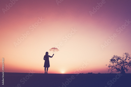 The silhouette of the lonely young woman holding an umbrella on the cliff at the sunset