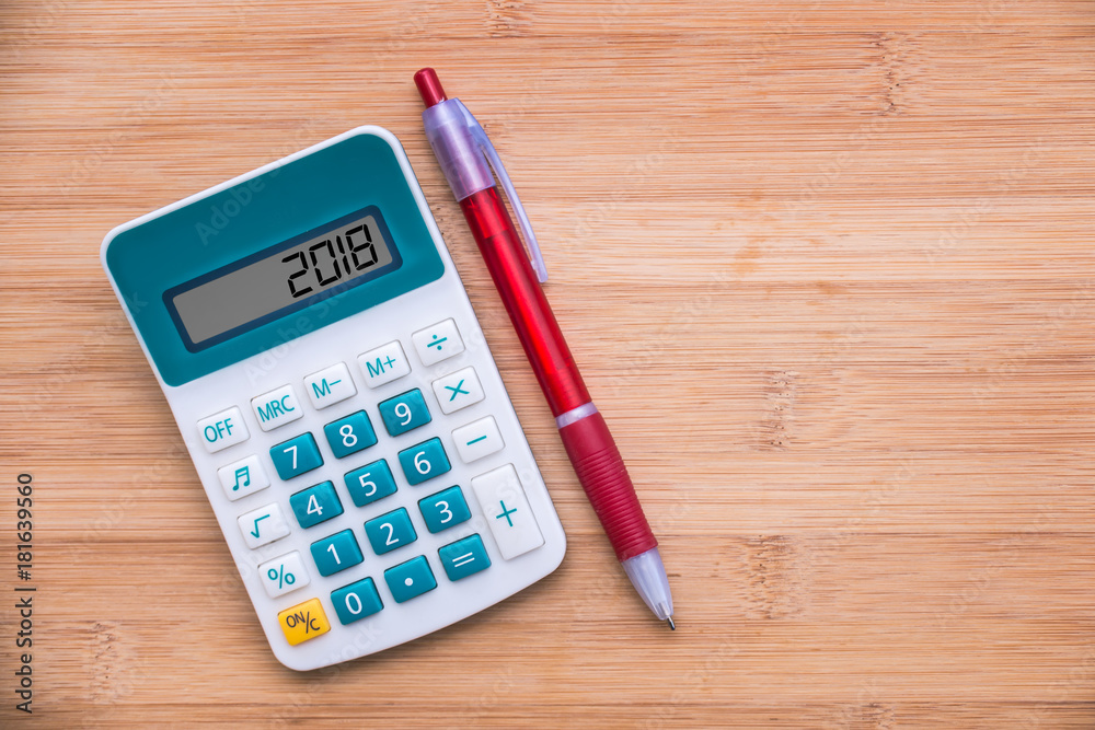 2018 written on a calculator and a pen on wooden background 2018 written on a calculator and a pen on wooden background