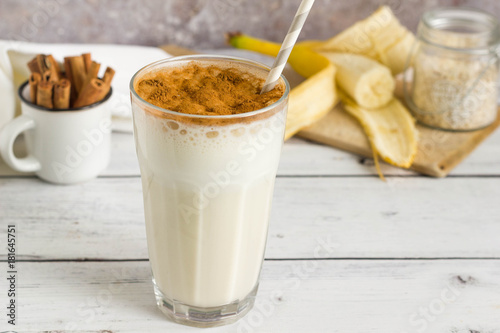 Banana oat milkshake with cinnamon on top, served on wooden table
