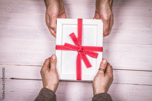 Fotografie Man's and woman's hands exchanging a gift wrapped blank frame over a wooden back