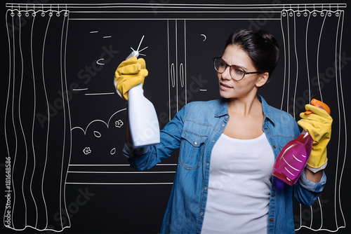 Nice one. Pleasant delighted woman holdign sprays and using them while doign spring cleaning photo