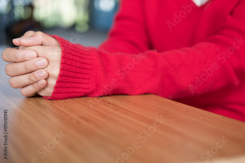 woman wearing red sweater folding her hands together on wood table. girl clasped hands together while praying