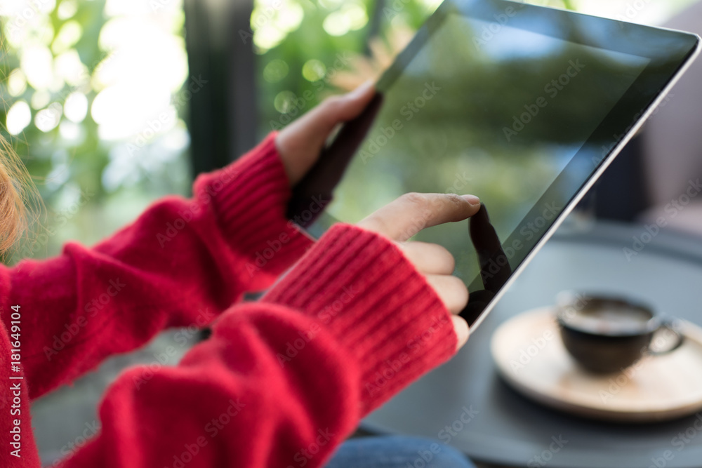 woman wearing red sweater typing text message on application on tablet at home. female adult sitting on armchair using touchpad for social networking at cafe. technology, lifestyle, people