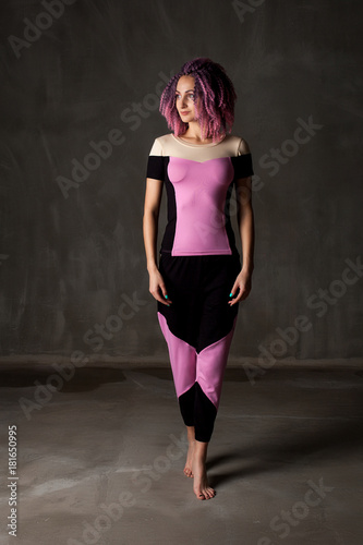 young girl with pink, curly hair in a suit for yoga on a black background
