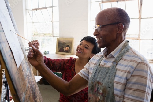 Smiling woman assisting male friend while painting photo