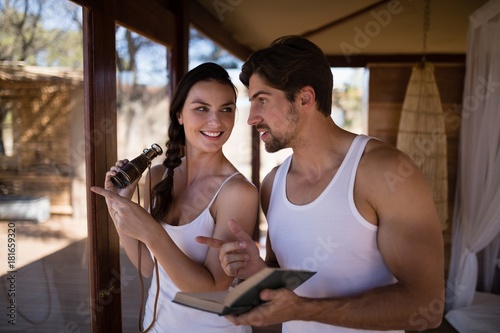 Couple holding binoculars while reading novel during safari