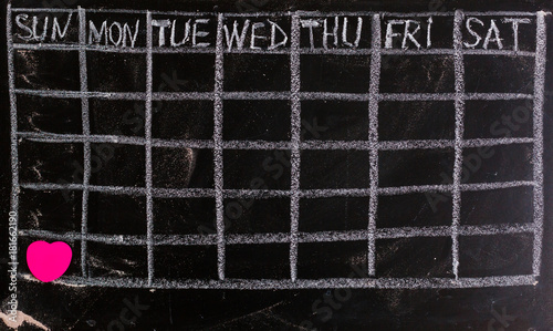 Freehand white chalk doodle sketch of blank monthly grid timetable schedule on black chalkboard