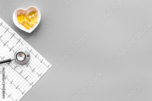 Treat heart. Pills in bowl in shape of heart, stethoscope and cardiogram on grey background top view copyspace photo