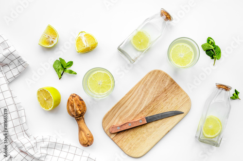 Prepare refreshing beverage lemonade. Lemons, juicer, bottle, knife, cutting board on white background top view