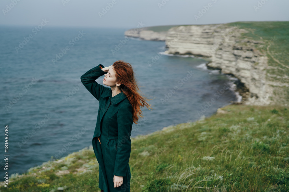 Beautiful young woman standing on a cliff above the sea, mountains, nature Beautiful young woman standing on a cliff above the sea, mountains, nature