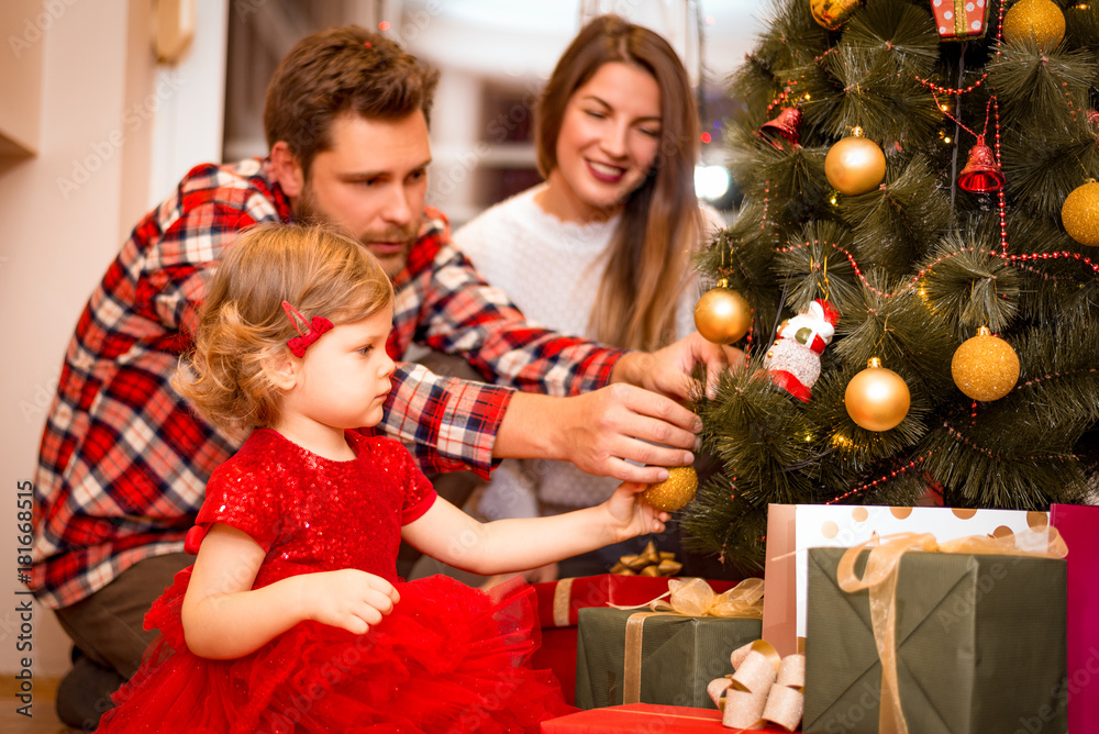 Happy family decorating a Christmas tree with boubles in the living-room Happy family decorating a Christmas tree with boubles in the living-room