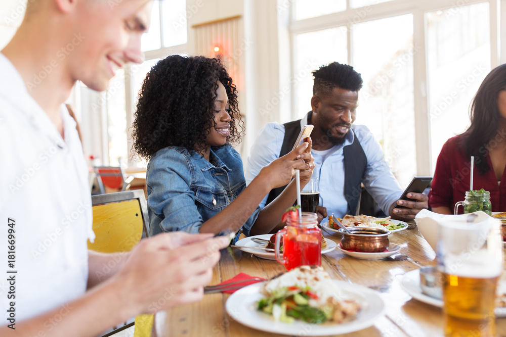 happy friends with smartphones at restaurant