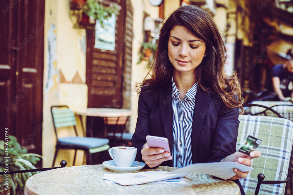 Woman at cafe, using phone to check credit card. Woman at cafe, using phone to check credit card.