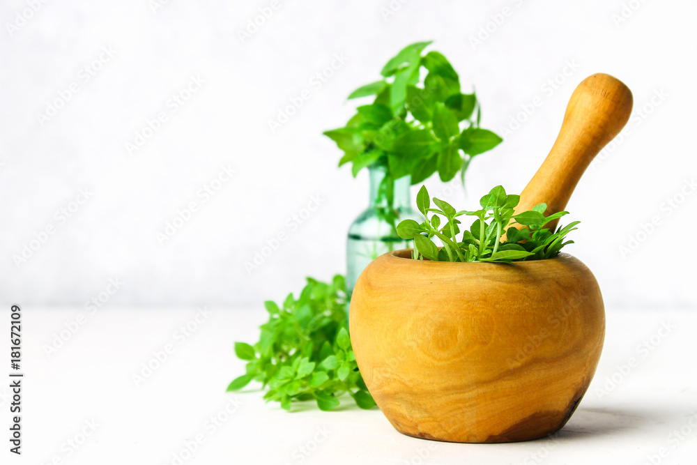 Green lemon basil in a wooden mortar on a light background. Behind the basil in the bottle.