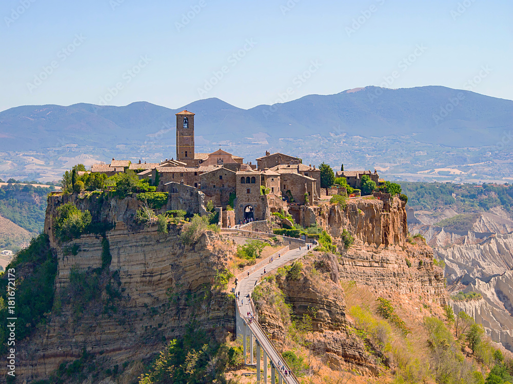 view of the beautiful Civita di Bagnoregio, Italy, with the famous bridge below and the mountains in the background