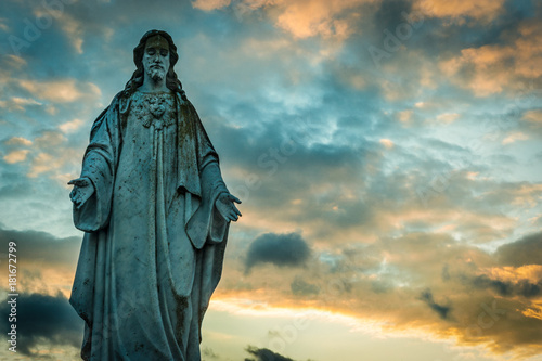 Old grungy and worn statue of Jesus in a cemetery at sunset