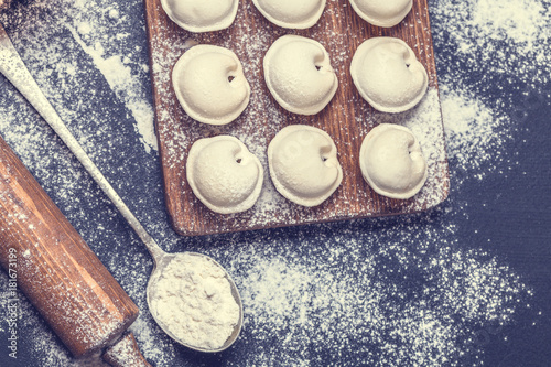 Fototapeta Naklejka Na Ścianę i Meble -  Raw dumplings on a black background, flour, rolling pin, spoon, horizontally, flat lay